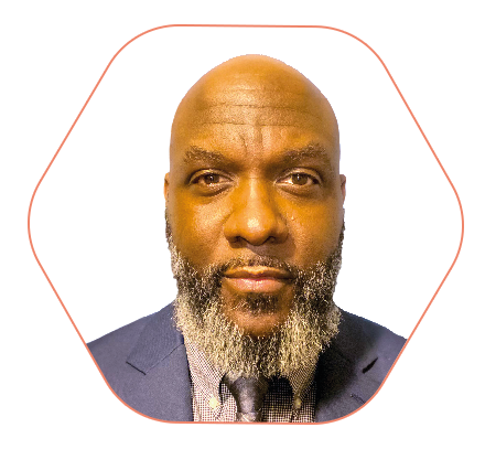 Close-up portrait of a bald man with a gray beard wearing a navy suit and patterned tie, looking at the camera.